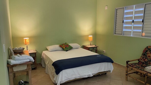 Une chambre bien rangée, avec un lit, deux tables de chevet, une chaise et une fenêtre équipée de stores.