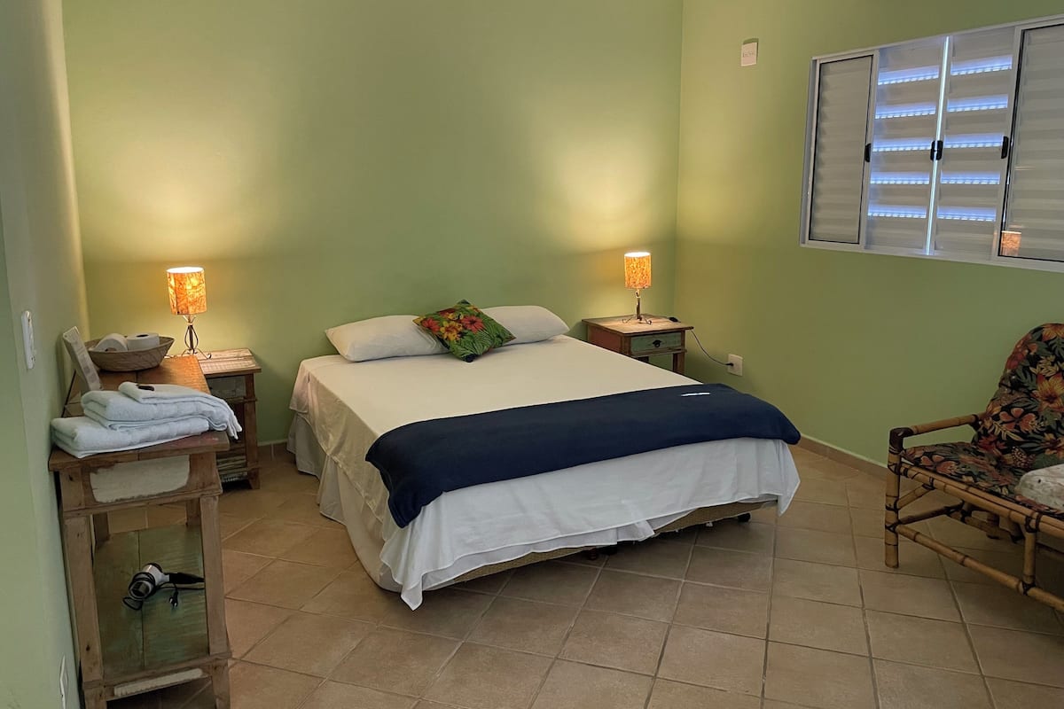 A neatly arranged bedroom with a bed, two bedside tables, a chair, and a window with blinds.