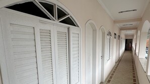 Un largo pasillo con puertas y ventanas blancas, piso de baldosas y una lámpara en el techo.