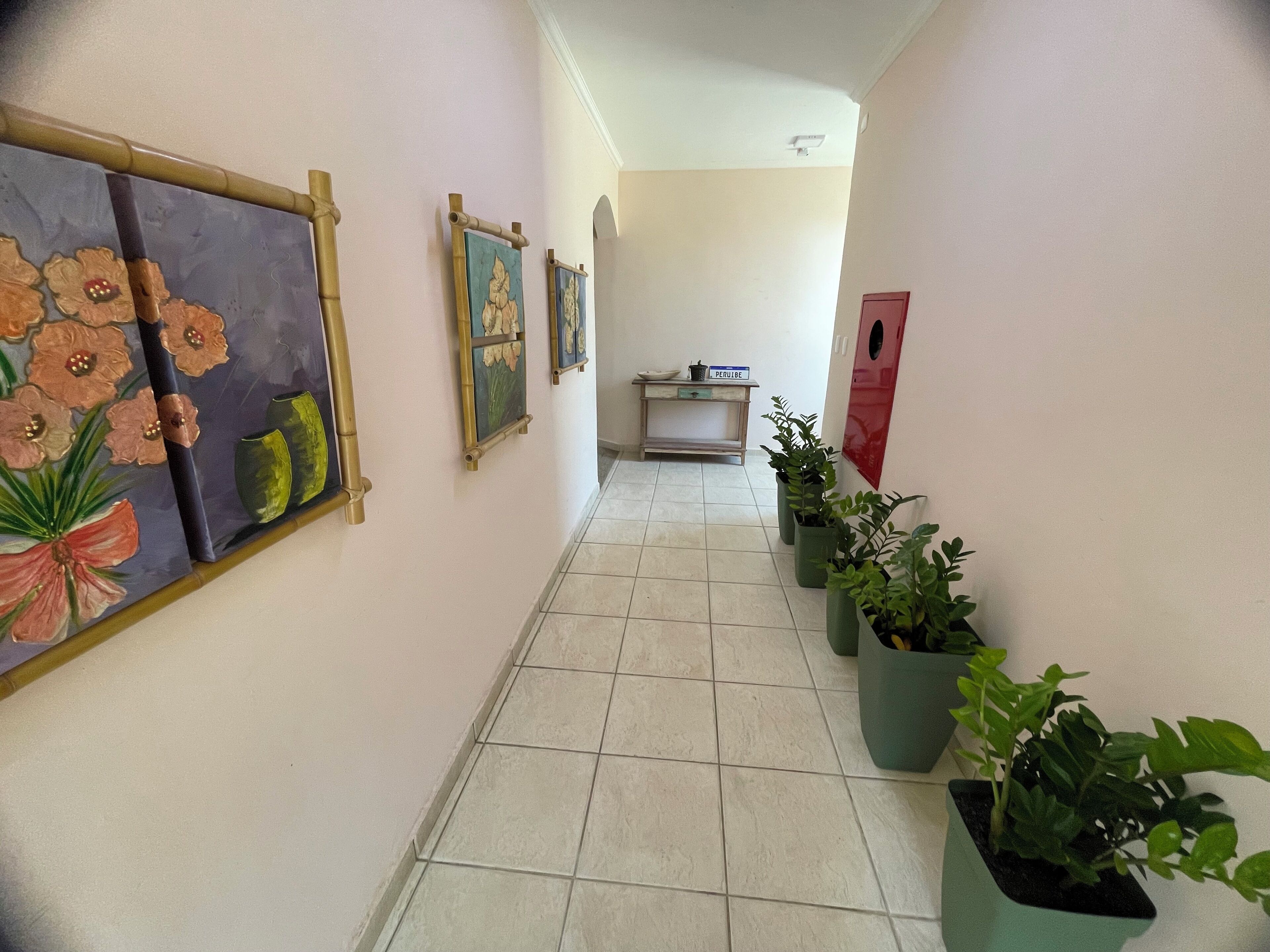 Un pasillo con suelo de baldosas, obras de arte colgadas en la pared y plantas en macetas.