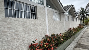 Un edificio moderno con paredes de textura pétrea, ventanas grandes con persianas y un cantero con flores rojas y amarillas a lo largo de la acera.