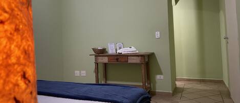 Una habitación con una cama, una pequeña mesa de madera con una cesta y toallas, y una puerta que conduce a otra habitación.