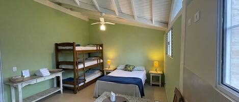 A room with bunk beds, a small table with a towel and a cup, and a window with blinds.