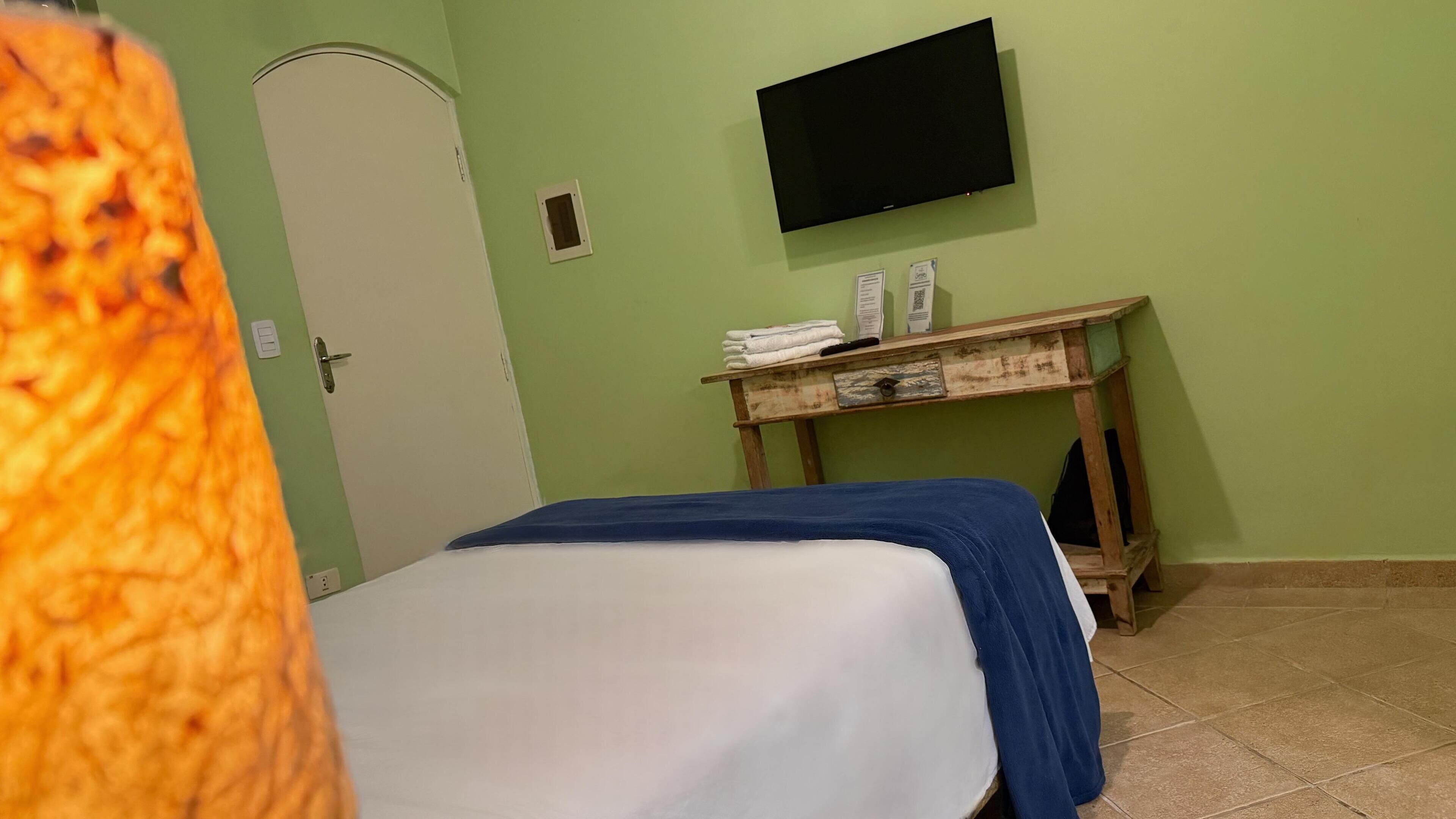 A room with a bed, a wooden nightstand, a television mounted on the wall, and a door.
