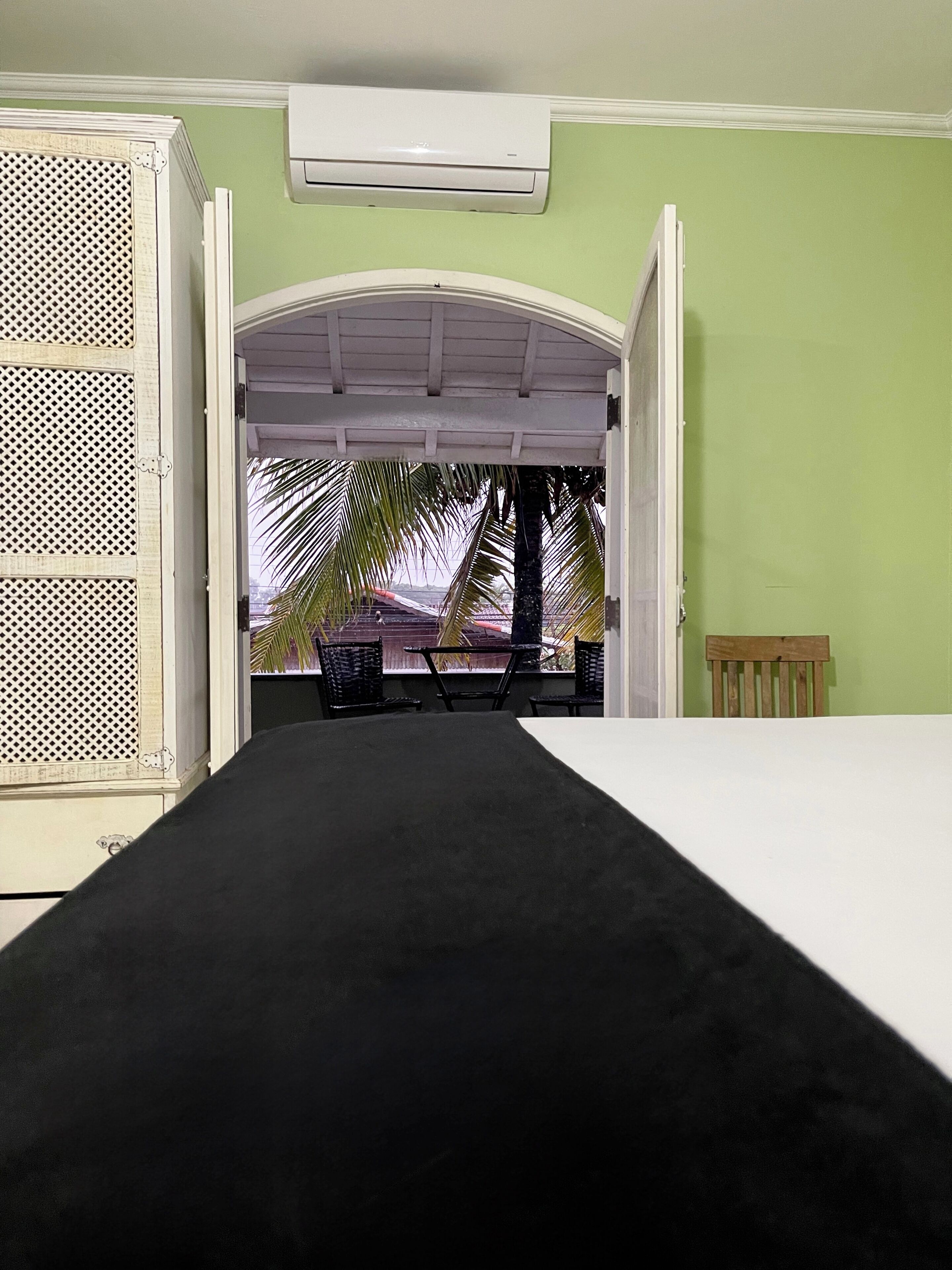 Une chambre avec un lit, une porte ouverte donnant sur un espace extérieur abrité, équipé d’une table et de chaises, et un appareil de climatisation fixé au mur.