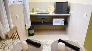 Una cocina compacta equipada con microondas, lavamanos y un refrigerador pequeño.