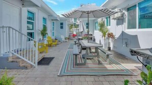 A covered outdoor patio with a dining table and chairs, a striped umbrella, and potted plants. - Hollywood Beach Escapade Studio w/ Free Parking (Hollywood)