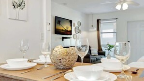 A dining table set with white plates, bowls, and wine glasses, with a woven basket in the center. - Hollywood Beach Escapade Studio w/ Free Parking (Hollywood)