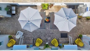 A rooftop terrace with two large striped umbrellas, yellow lounge chairs, and a pool area. - Hollywood Beach Escapade Studio w/ Free Parking (Hollywood)