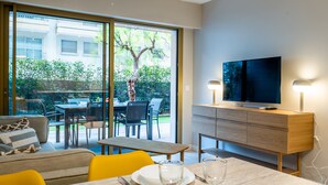 A modern living room with a dining area, a television, and a view of a garden through large sliding doors. - Downtown Cannes, Apartment with Garden (Cannes)