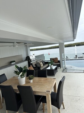 Un patio exterior con una mesa de comedor, sillas, una parrilla y una zona de estar con vistas a un cuerpo de agua.