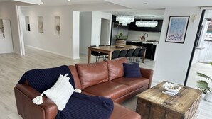 Un salon moderne avec un canapé en cuir marron, une table basse en bois et, au fond, un coin repas.