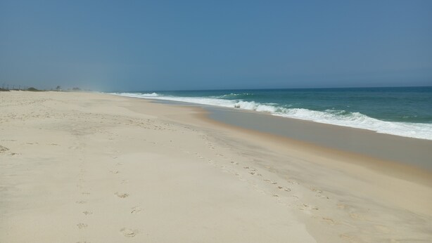 A wide sandy beach with gentle waves and a clear blue sky.