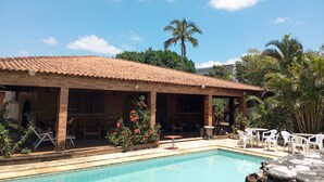 A poolside area with a tiled roof structure, a swimming pool, and outdoor seating.