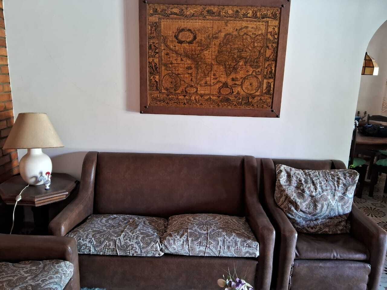 Um sofá de couro marrom com almofadas estampadas, uma pequena mesa lateral com abajur e um mapa grande emoldurado na parede.