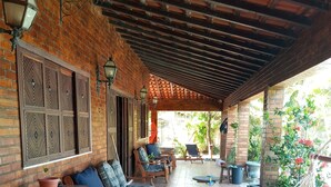 A covered patio area with brick walls, patterned floor tiles, wooden furniture, and hanging chairs.