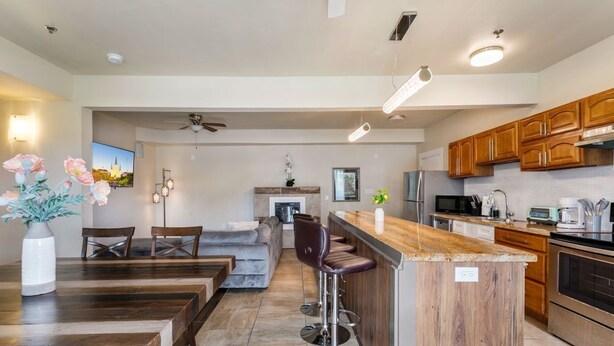 A modern kitchen with wooden cabinets, a central island with bar stools, a dining area with a sofa, and a TV mounted on the wall. - Spacious Urban Living Near French Quarter (New Orleans)