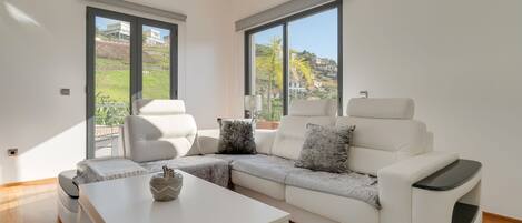 Una sala de estar moderna con un sofá seccional blanco, una mesa de centro blanca y un ventanal con vistas a una ladera.