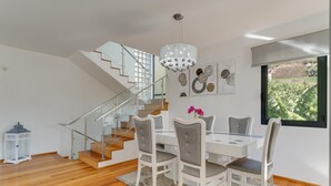A dining area with a glass table, white chairs, a chandelier, and a staircase. - Countryside Charm  (Camara de Lobos)