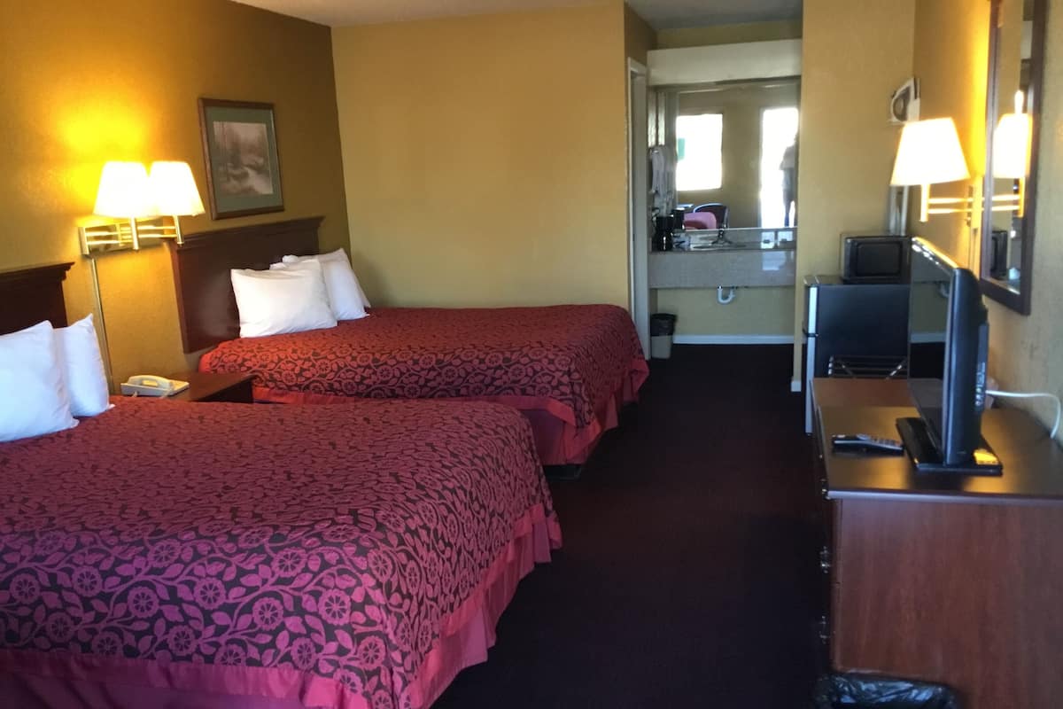 Une chambre d’hôtel avec deux lits, un bureau équipé d’un ordinateur et d’une télévision, un miroir et une poubelle.