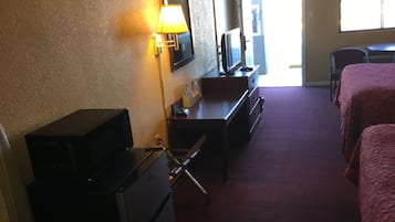 A hotel room with a desk, a television, a dresser, and two beds.