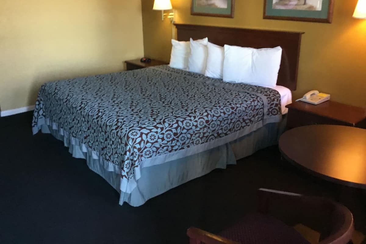 Une chambre d’hôtel avec un grand lit, une table de chevet avec une lampe, une table ronde et une chaise.