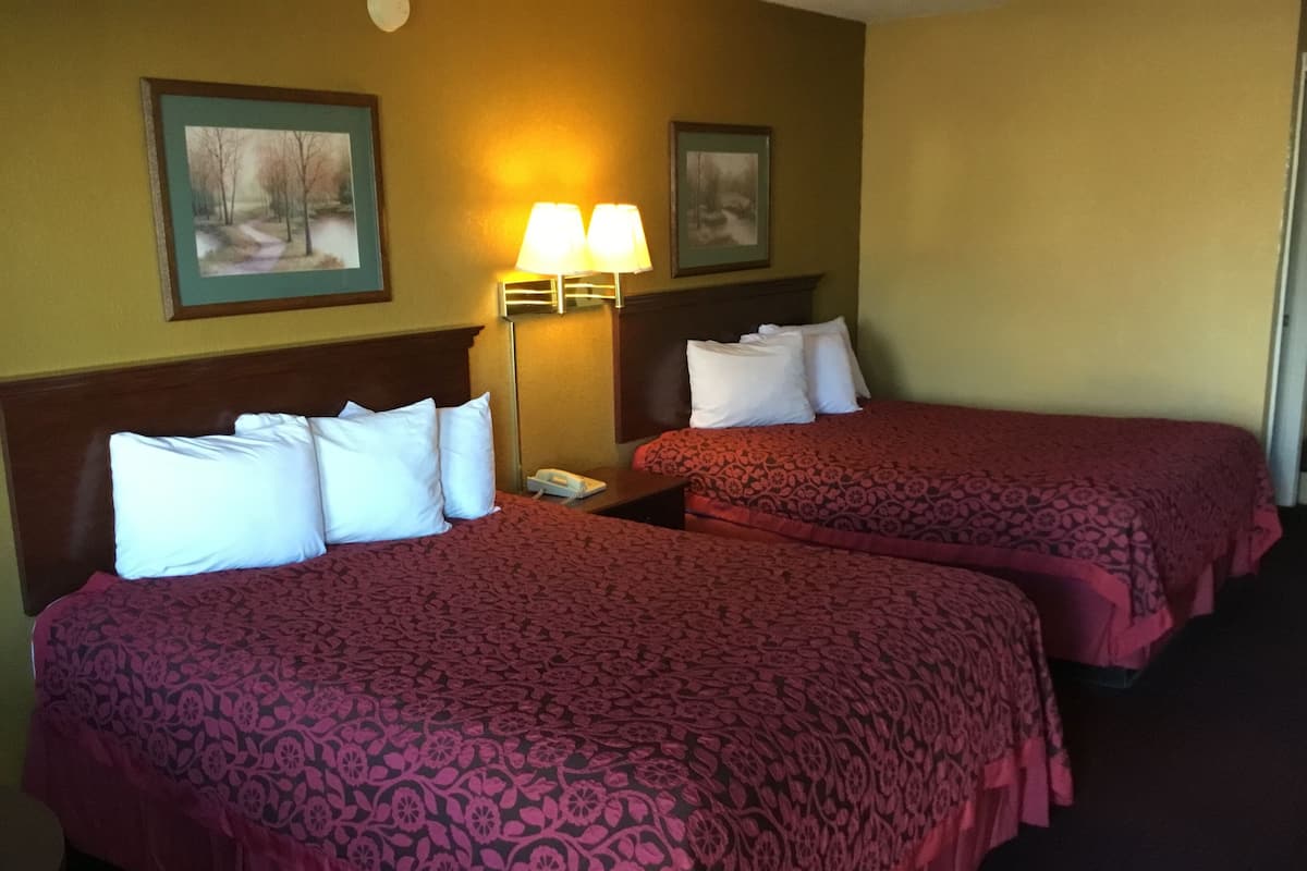 Une chambre d’hôtel avec deux lits, chacun recouvert d’une couvre-lit à motifs et agrémenté d’oreillers blancs. Une table de chevet avec une lampe et un téléphone se trouve entre les deux lits.