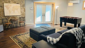Ein Wohnzimmer mit Steinwand, einer Weltkarte, einem Kicker, einem Sofa und einem Couchtisch.