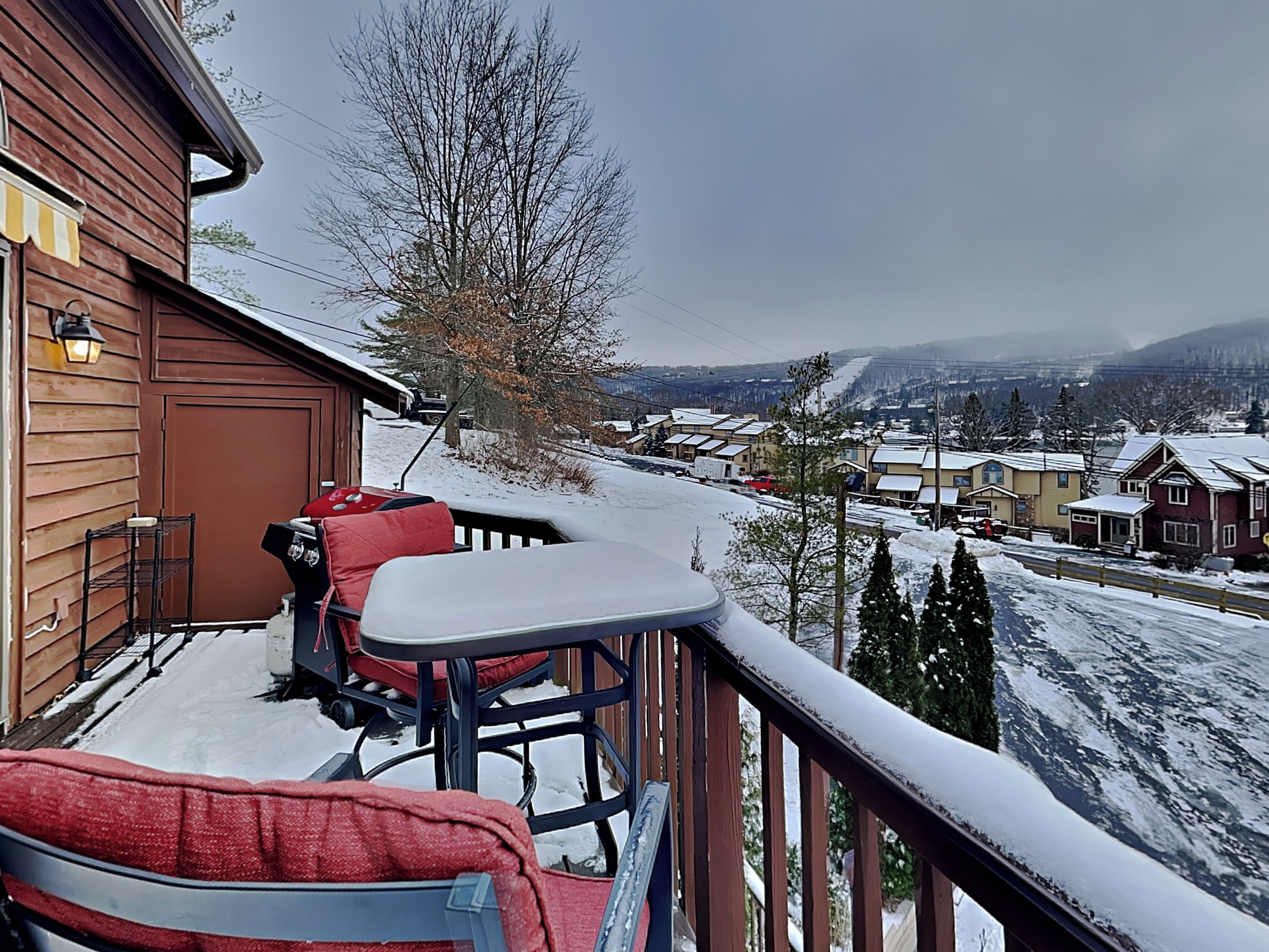 Eine Holzdielen-Terrasse mit Außenmöbeln, mit Blick auf eine verschneite Landschaft und Gebäude.
