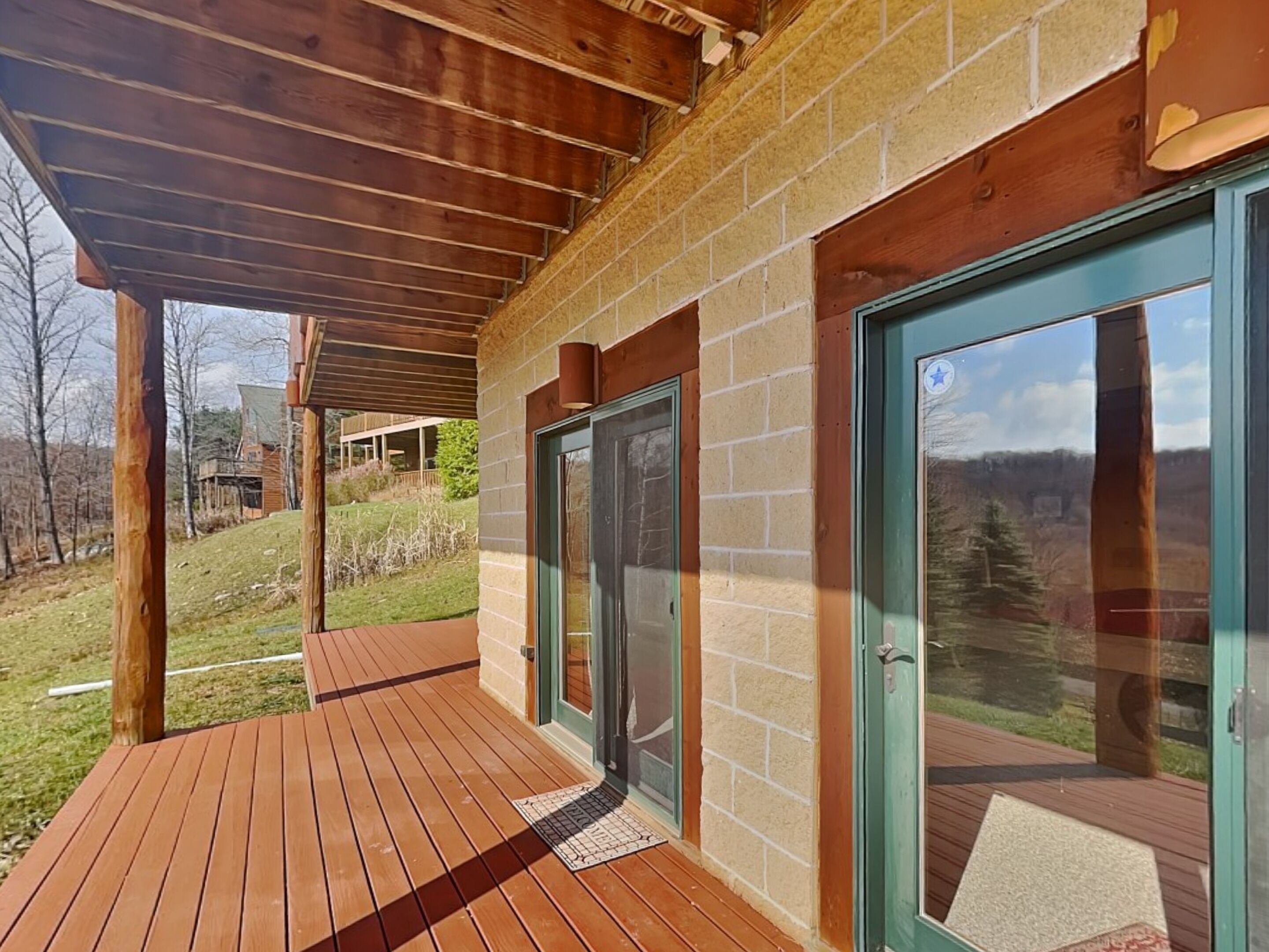 A wooden deck with a covered area, a brick wall, and a glass door leading to an outdoor space.