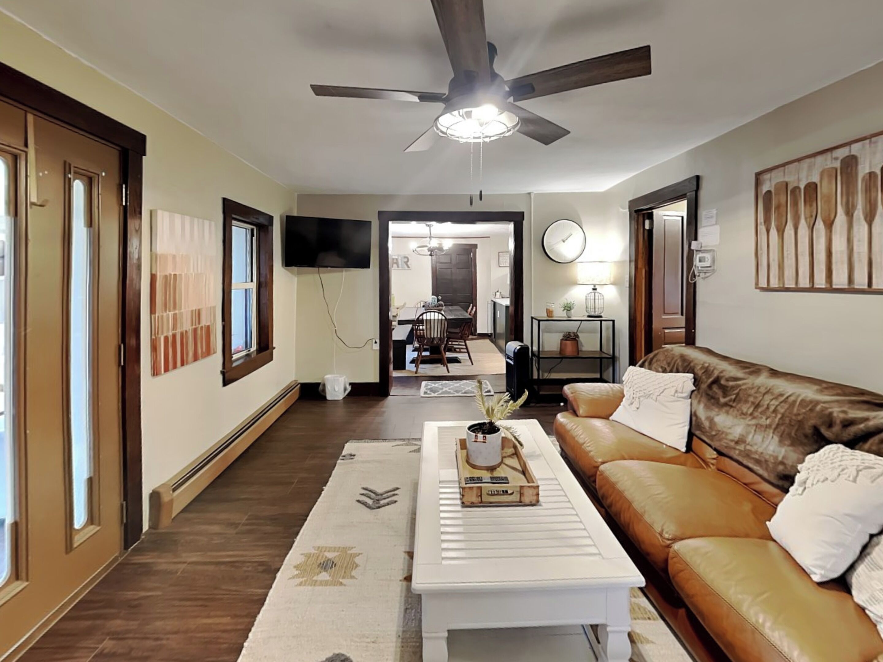 A living room with a ceiling fan, a TV, a sofa, a coffee table, and a dining area in the background.