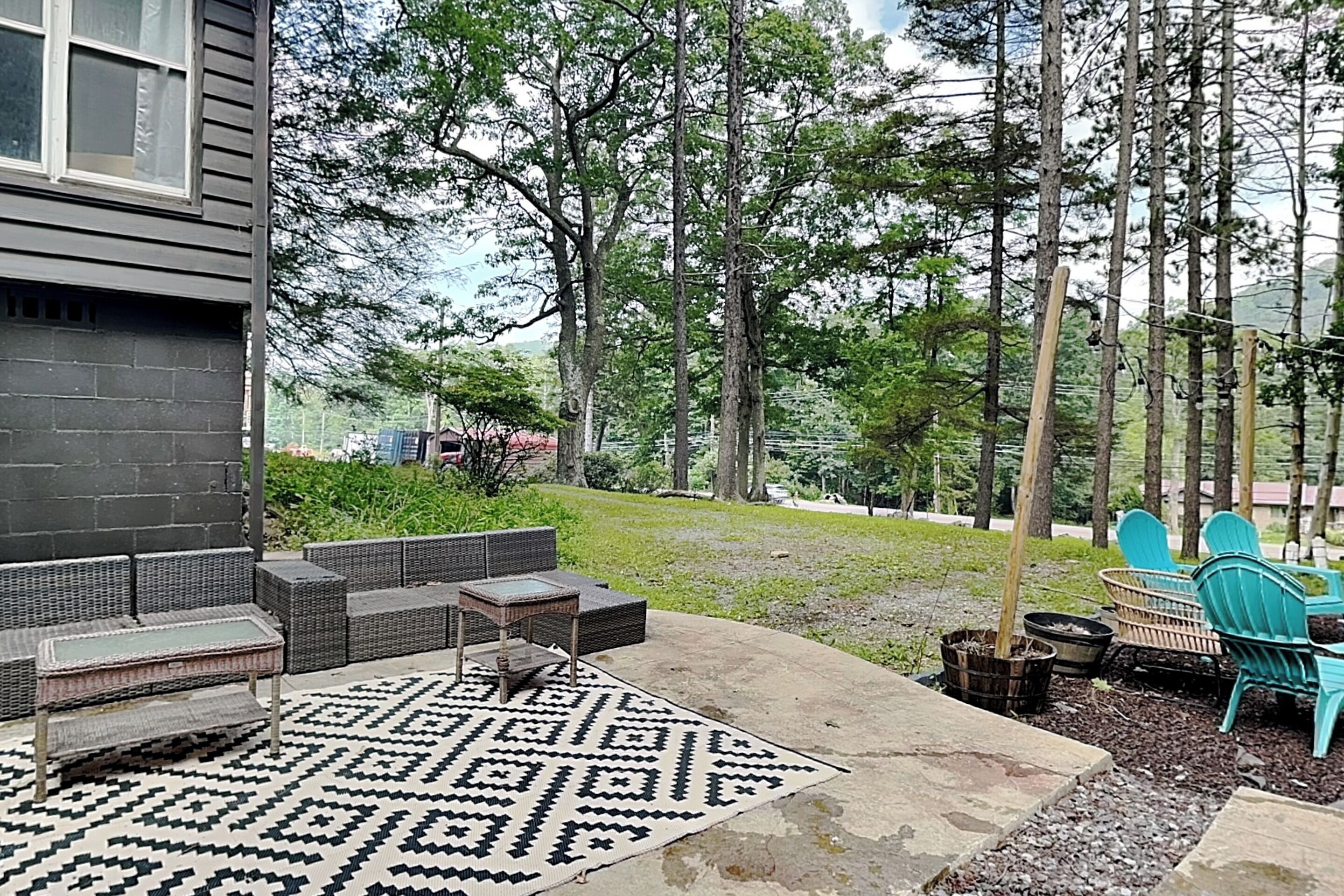 Eine Terrassenfläche mit Gartenmöbeln, einem gemusterten Teppich und Blick auf ein bewaldetes Gebiet.