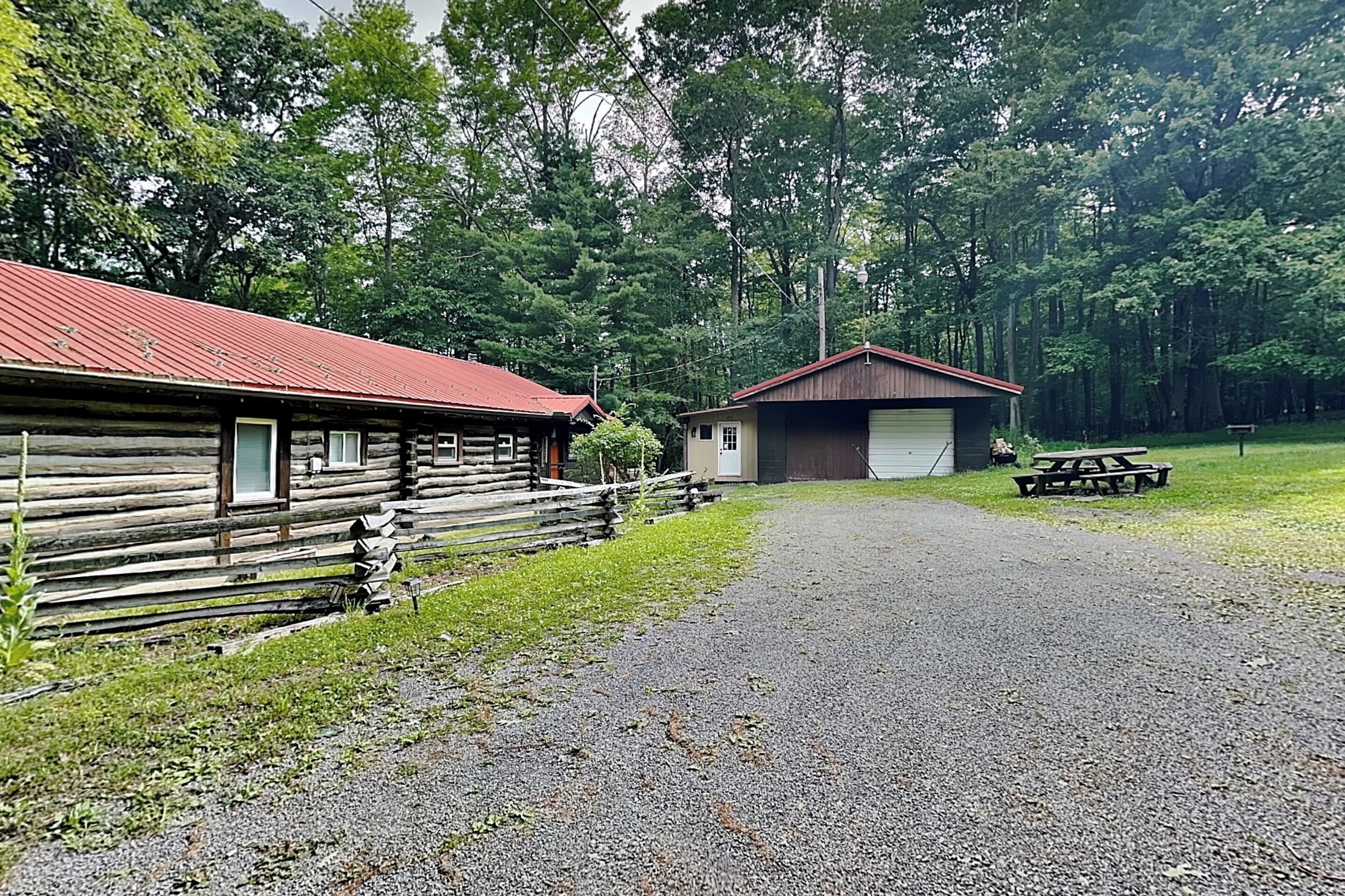 A rustic cabin with a gravel driveway leading to a picnic table.