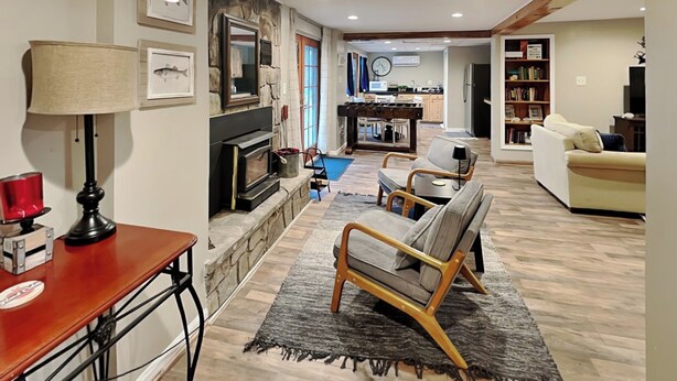 A living room with a fireplace, a sofa, a coffee table, and a dining area with a kitchen in the background. - The Whiskey Barrel Lodge by Taylor Made Deep Creek (Oakland)