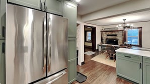 A kitchen with a stainless steel refrigerator, wooden flooring, and a stone fireplace. - The Whiskey Barrel Lodge by Taylor Made Deep Creek (Oakland)