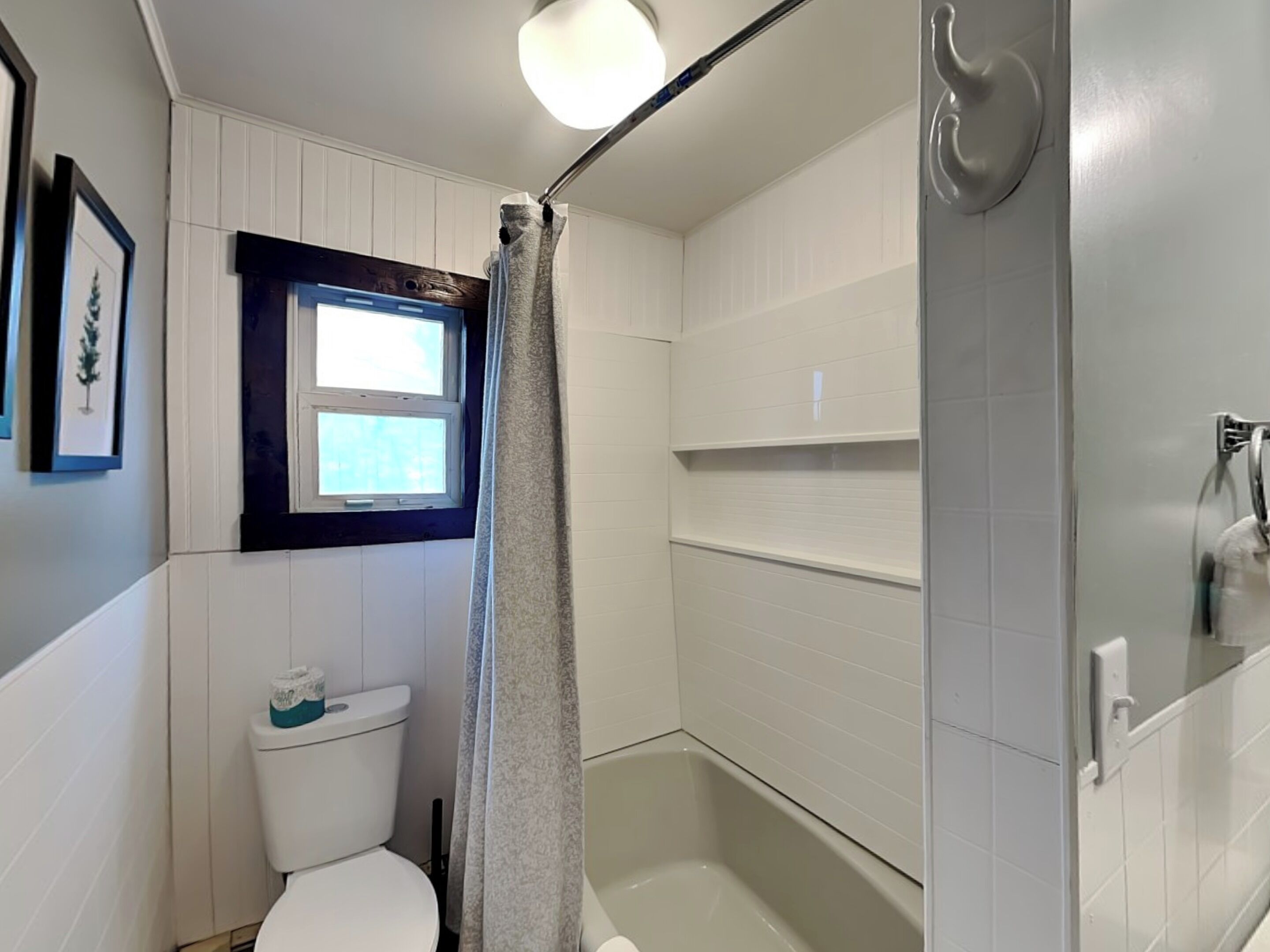 A bathroom with a toilet, a shower, a window, and a towel rack.