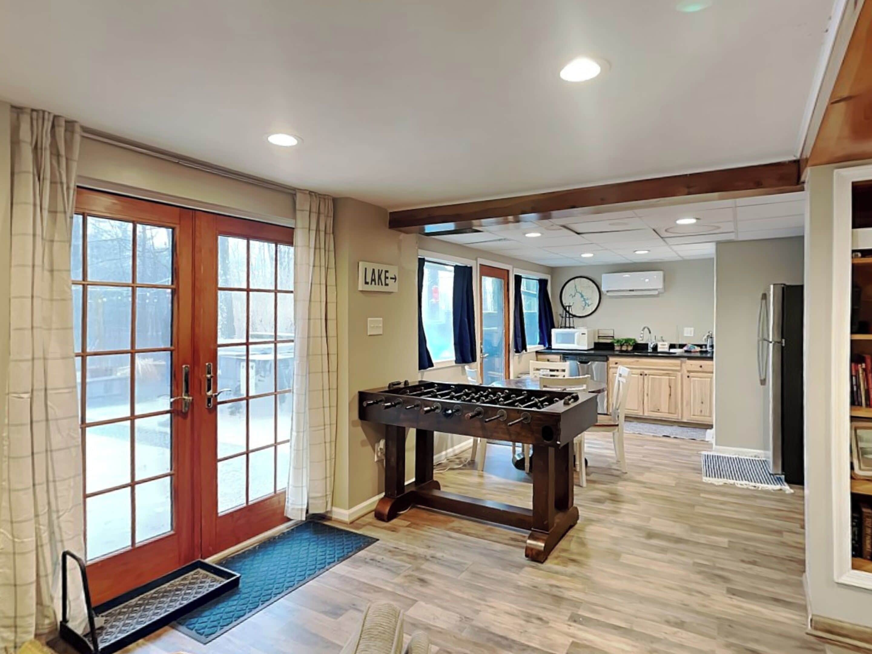 A spacious living area with a foosball table, a kitchen with modern appliances, and a view of a lake through large windows.