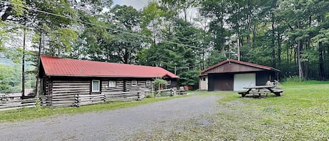 A rural property with a gravel driveway leading to a wooden cabin with a red roof and a smaller shed with a brown roof.