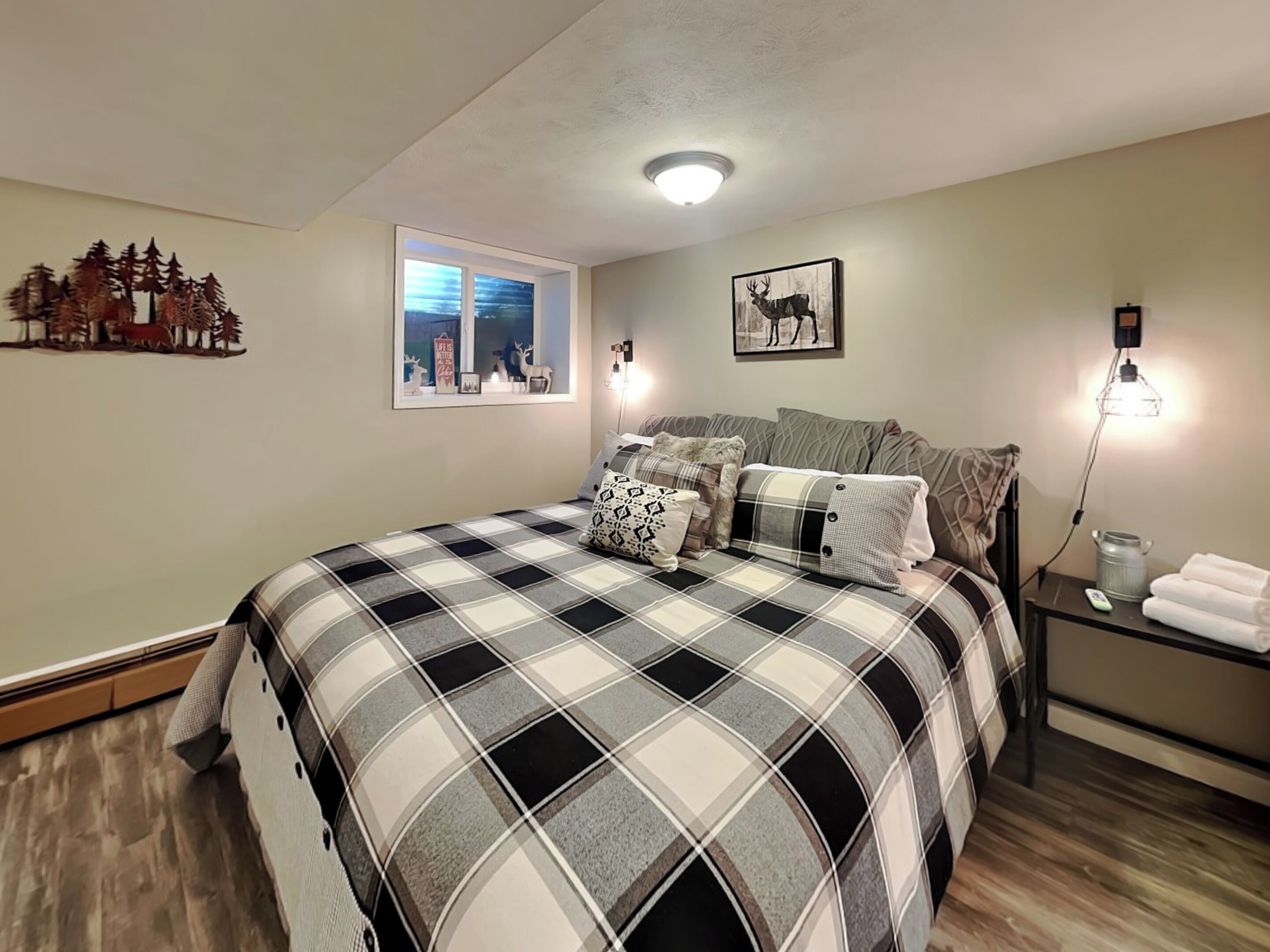 Une chambre à coucher comprenant un lit, une table de chevet, une lampe fixée au mur, une fenêtre avec vue et un élément décoratif mural.