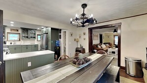 A modern kitchen with green cabinets, a central island, and a dining area with a wooden table. - The Whiskey Barrel Lodge by Taylor Made Deep Creek (Oakland)