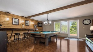 Une table de billard dans une pièce aux murs en bois, avec une horloge et un coin bar.