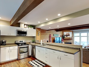 A modern kitchen with white cabinets, stainless steel appliances, a wooden accent wall, and a checkered floor rug. - Villages of Wisp 66 Bright Passage by Taylor Made Deep Creek (McHenry)