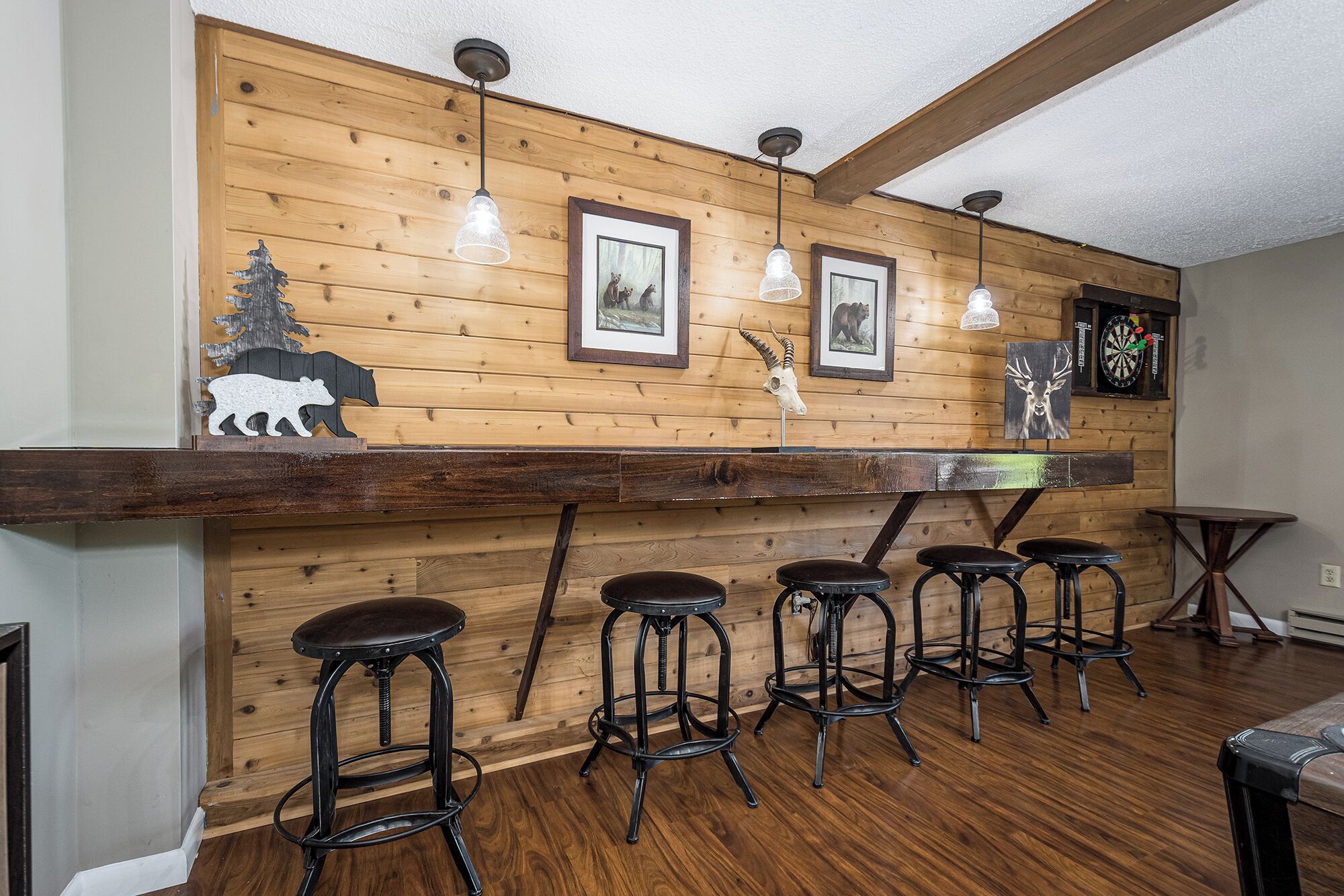 Una zona de bar rústica con paneles de madera, cuadros enmarcados de fauna y un dardo.