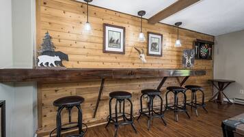 Una zona de bar rústica con paneles de madera, cuadros enmarcados de fauna y un dardo.