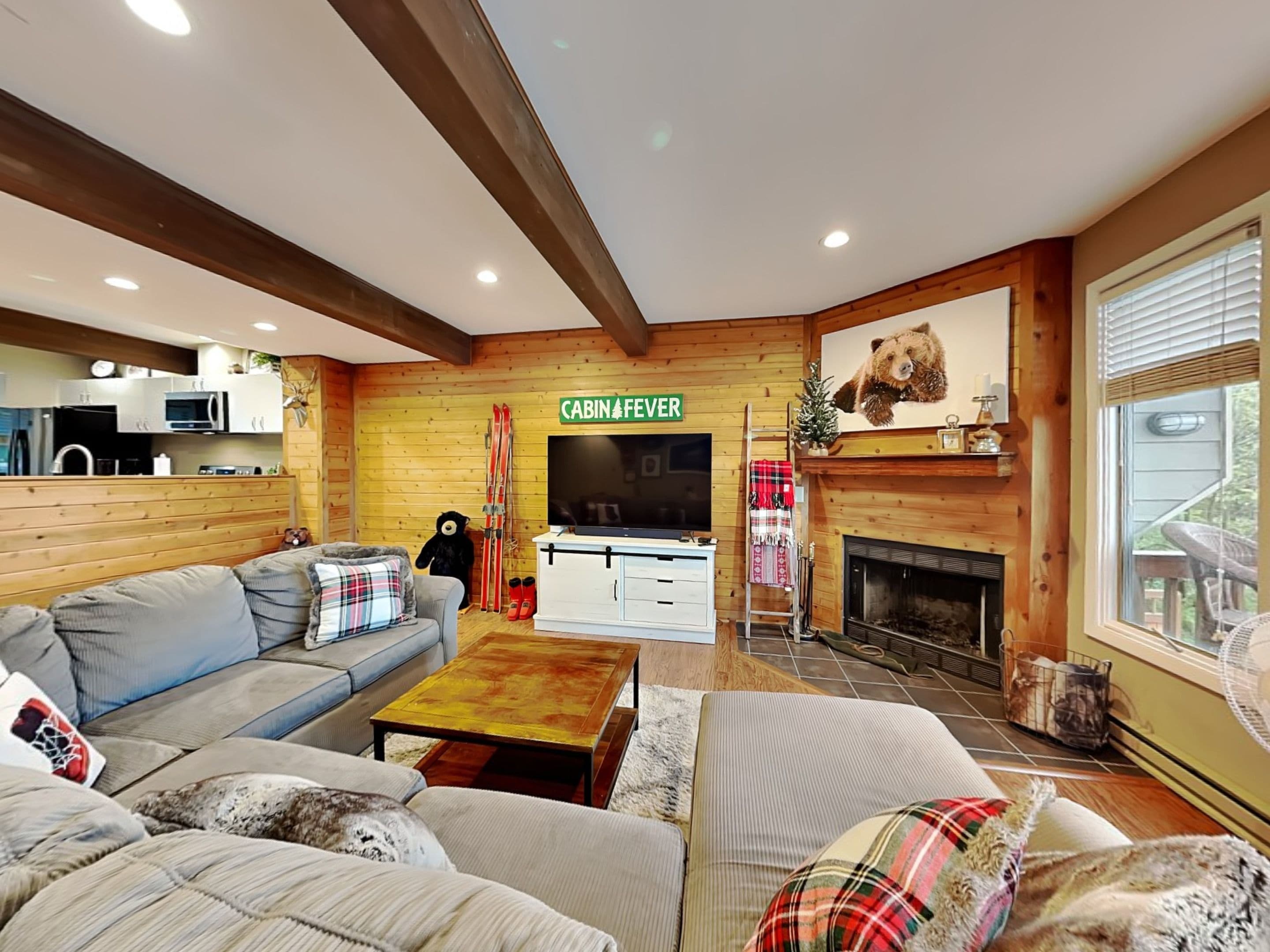 Un salón acogedor con chimenea, televisor y una cocina visible a través de una puerta abierta.