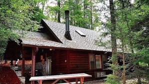 Ein rustikales Blockhaus mit Schornstein, einer Veranda und einem Picknicktisch in bewaldeter Landschaft.