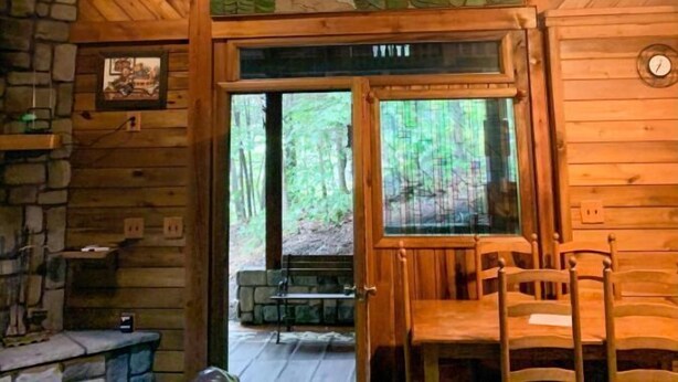 Ein rustikales Holzhütten-Interieur mit Deckenventilator, Steinwänden, einem Holzespeisesaal und einem großen Fenster mit Blick auf den Wald.