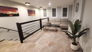 A modern living room with a staircase, a sofa, a coffee table, and a potted plant.