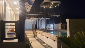 An outdoor swimming pool area with a covered seating area and steps leading to a door.