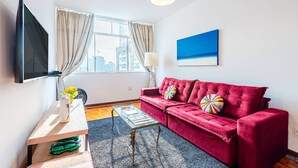 A modern living room with a red sofa, a flat-screen TV, a glass coffee table, and a large window with curtains. - Stylish & Charming in Consolação/Higienópolis • Parking • 3rd Guest Free (Sao Paulo)